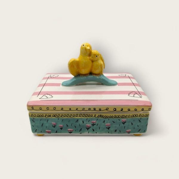 Hand-painted trinket box with twin golden canaries atop, amid blush stripes and mint floral patterns.
